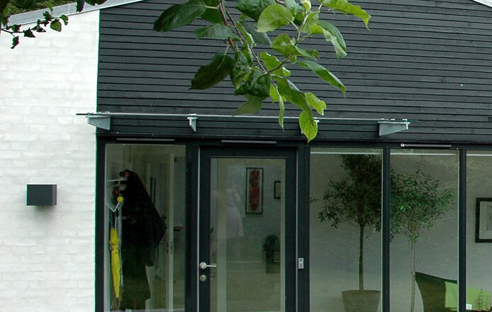 Foto af et indgangsparti i et renoveret hus i Horsens. Der er sorte trælister over et stort vinduesparti og pudset murstensvæg